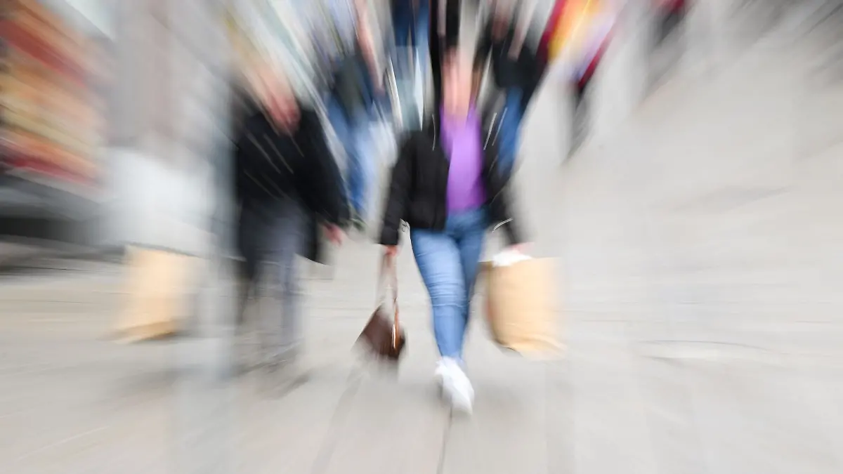 Passanten laufen mit Einkaufstüten durch eine Einkaufsstraße.