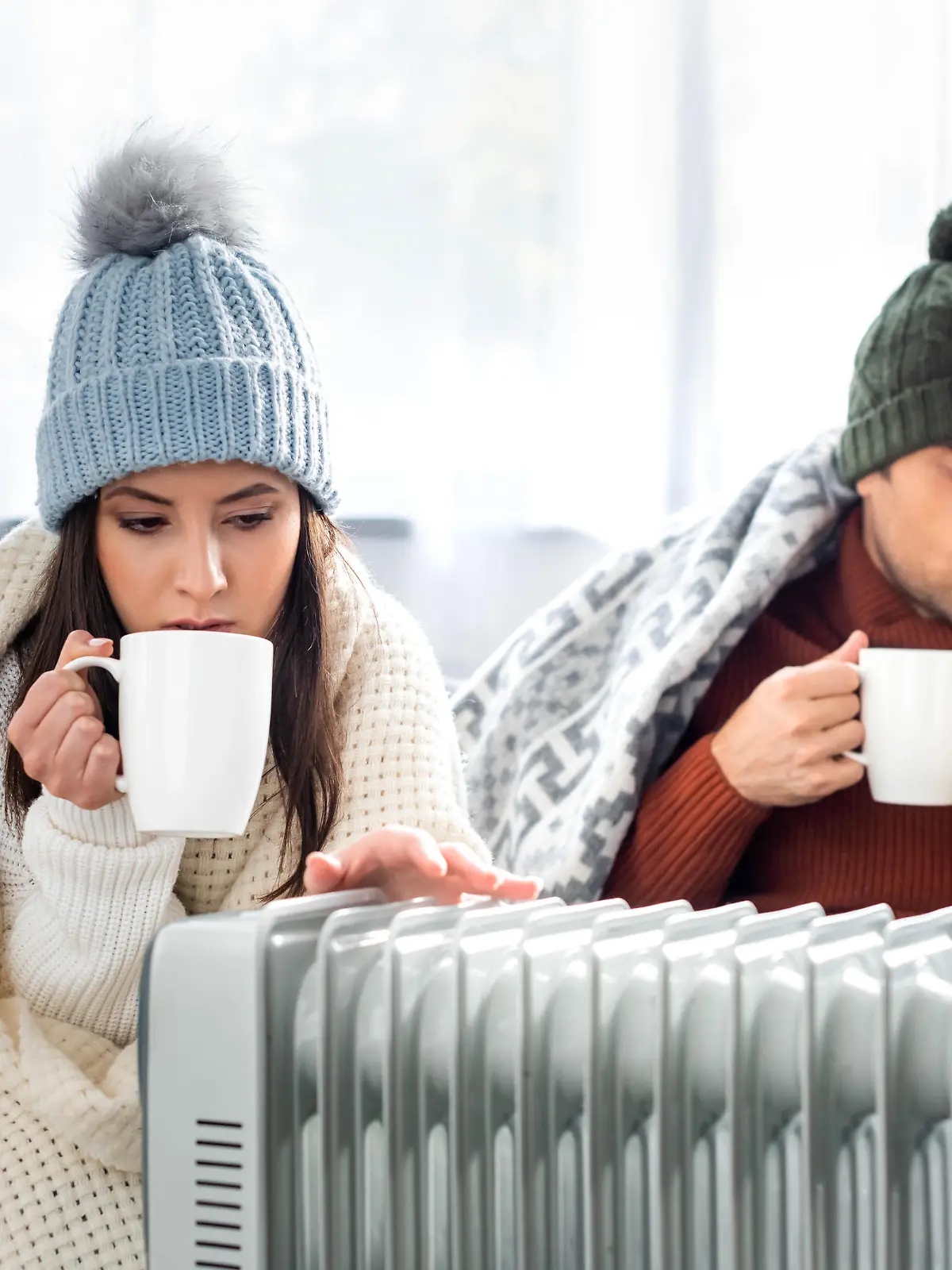 attractive girlfriend with cup of tea and boyfriend reading book and warming up near heater