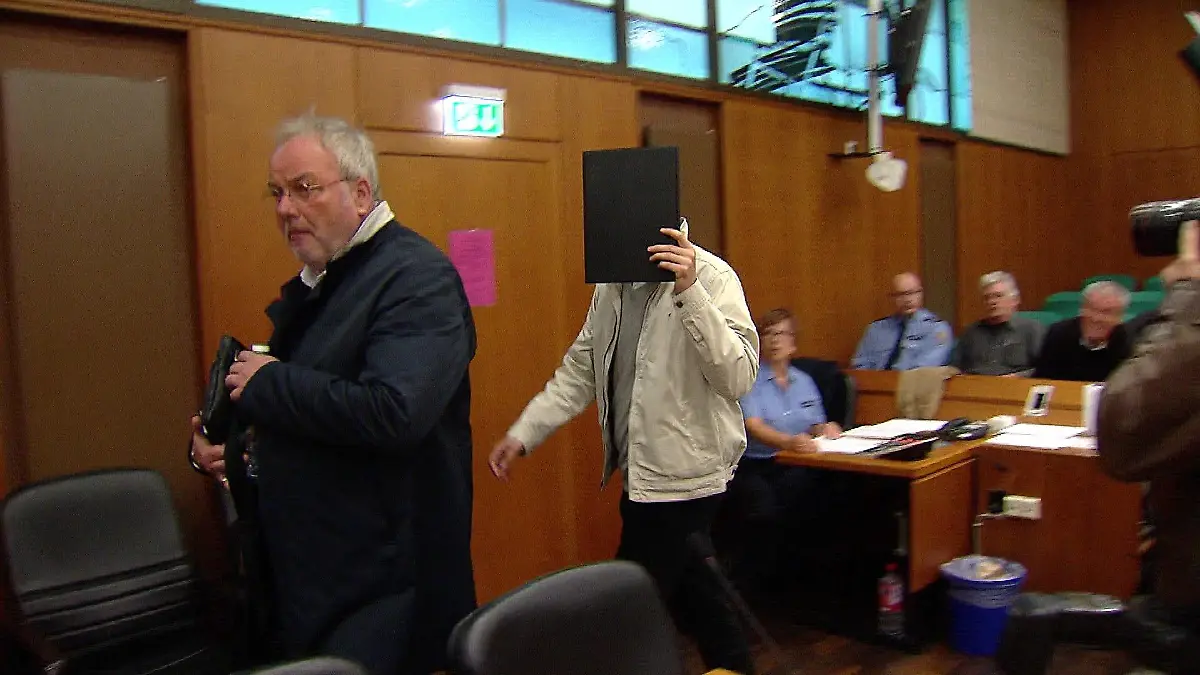 Der Angeklagte hält sich einen Ordner vor das Gesicht.