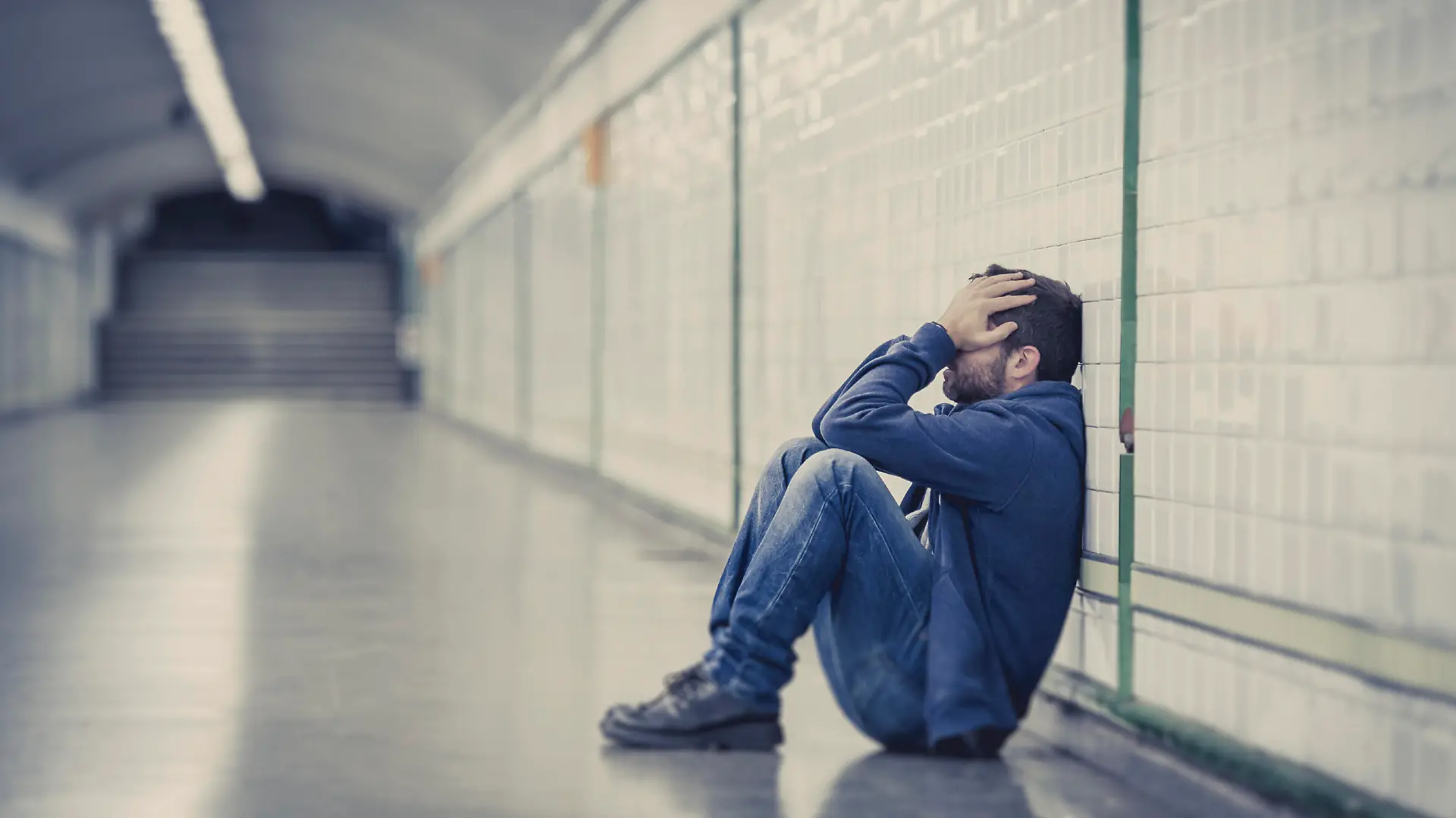 Young man abandoned lost in depression sitting on ground street subway tunnel suffering emotional pain, sadness and looking destroyed and desperate leaning on wall alone