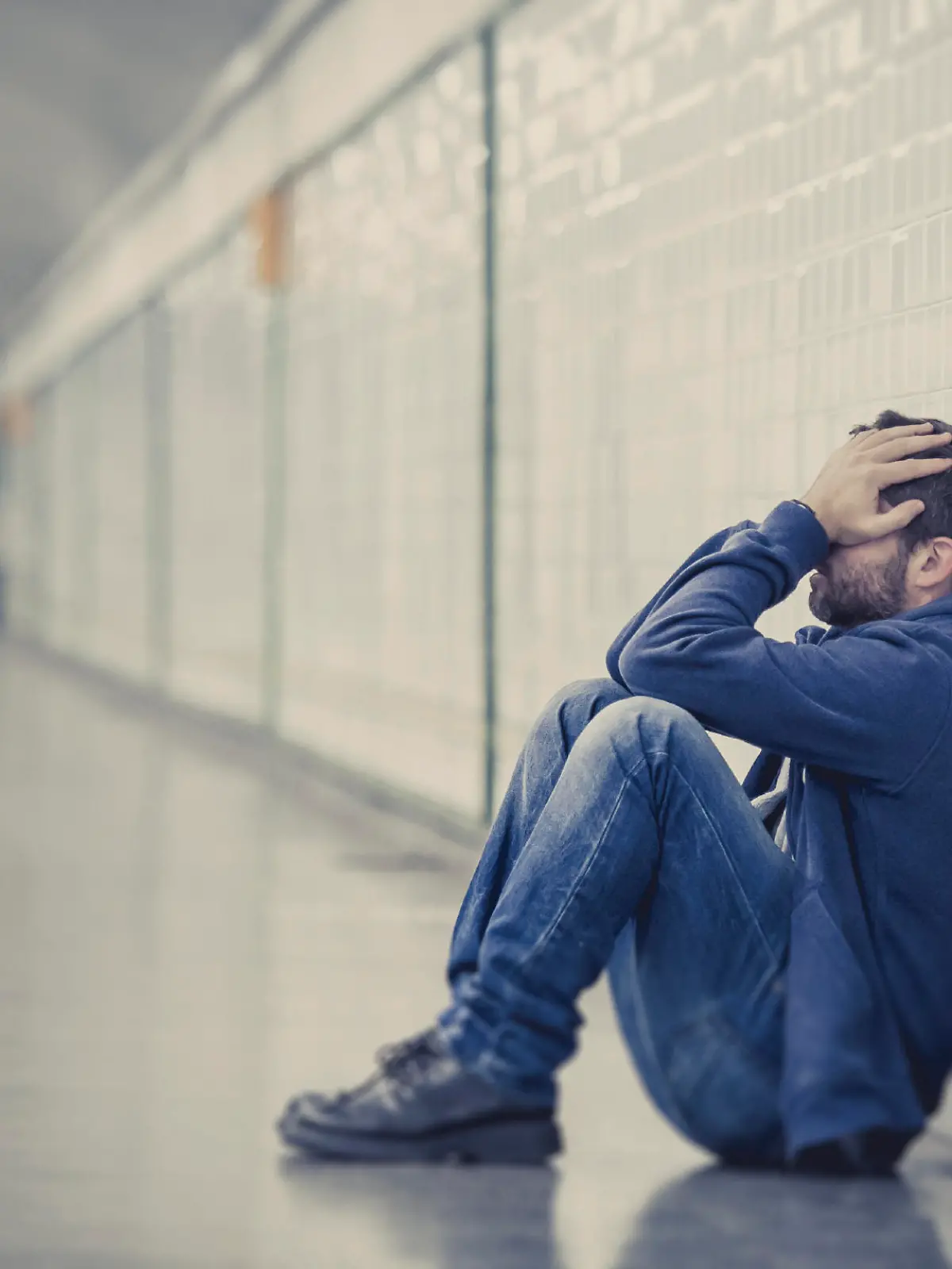 Young man abandoned lost in depression sitting on ground street subway tunnel suffering emotional pain, sadness and looking destroyed and desperate leaning on wall alone 