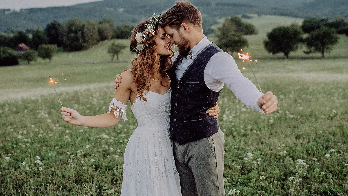 Beautiful young bride and groom with sparklers hugging outside in green nature.