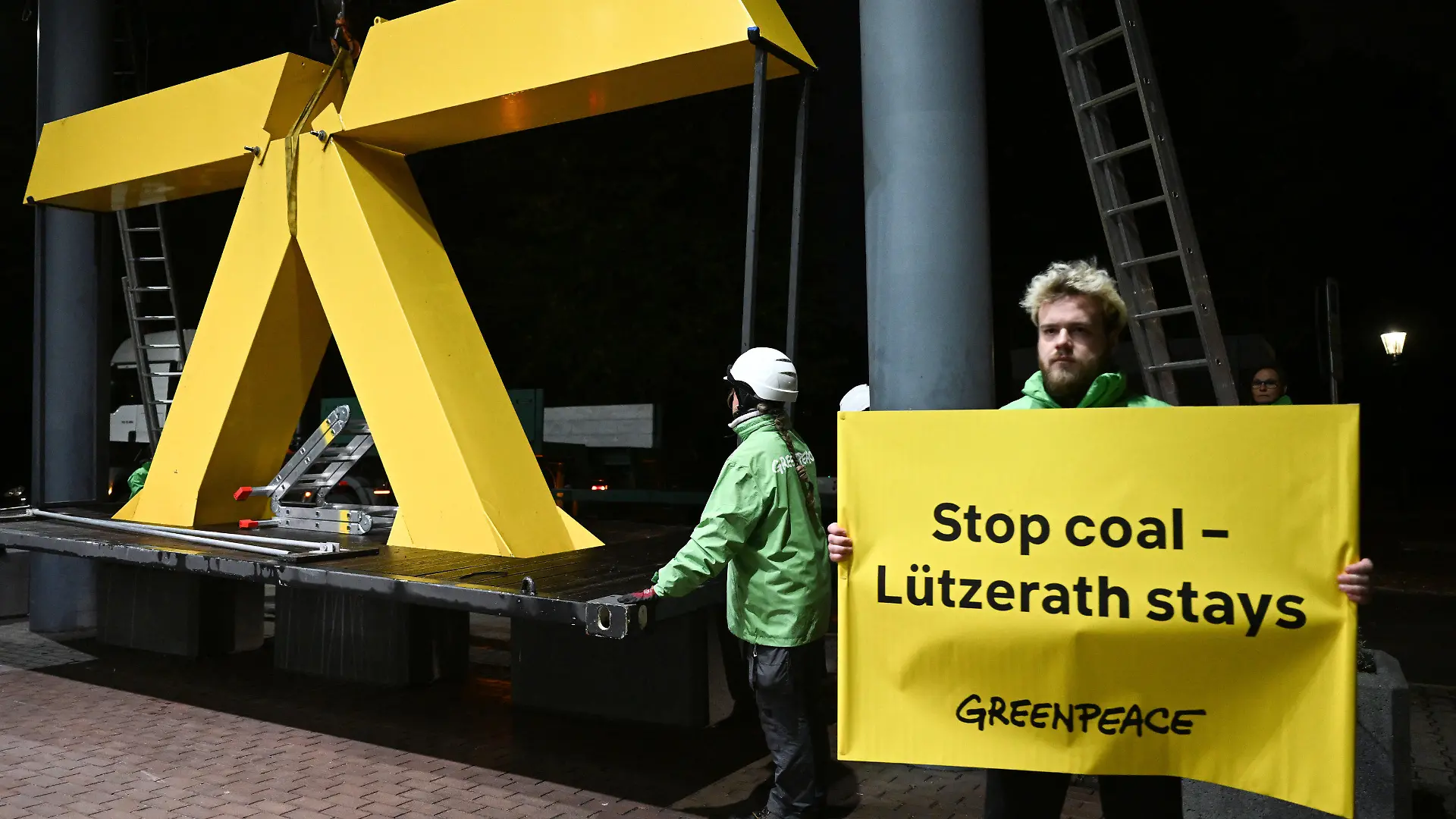 28.09.2022, Nordrhein-Westfalen, Düsseldorf: Greenpeace-Aktivisten bauen ein gelbes X vor dem nordrhein-westfälischen Wirtschaftsministerium auf. Ein Aktivist hält ein Plakat mit der englischen Aufschrift "Stoppt die Kohle - Lützerath bleibt!". Mit einer Aktion vor dem Wirtschaftsministerium hat die Umweltorganisation Greenpeace den Erhalt des verlassenen Braunkohleorts Lützerath am Rand des Tagebaus Garzweiler gefordert. Foto: Federico Gambarini/dpa +++ dpa-Bildfunk +++