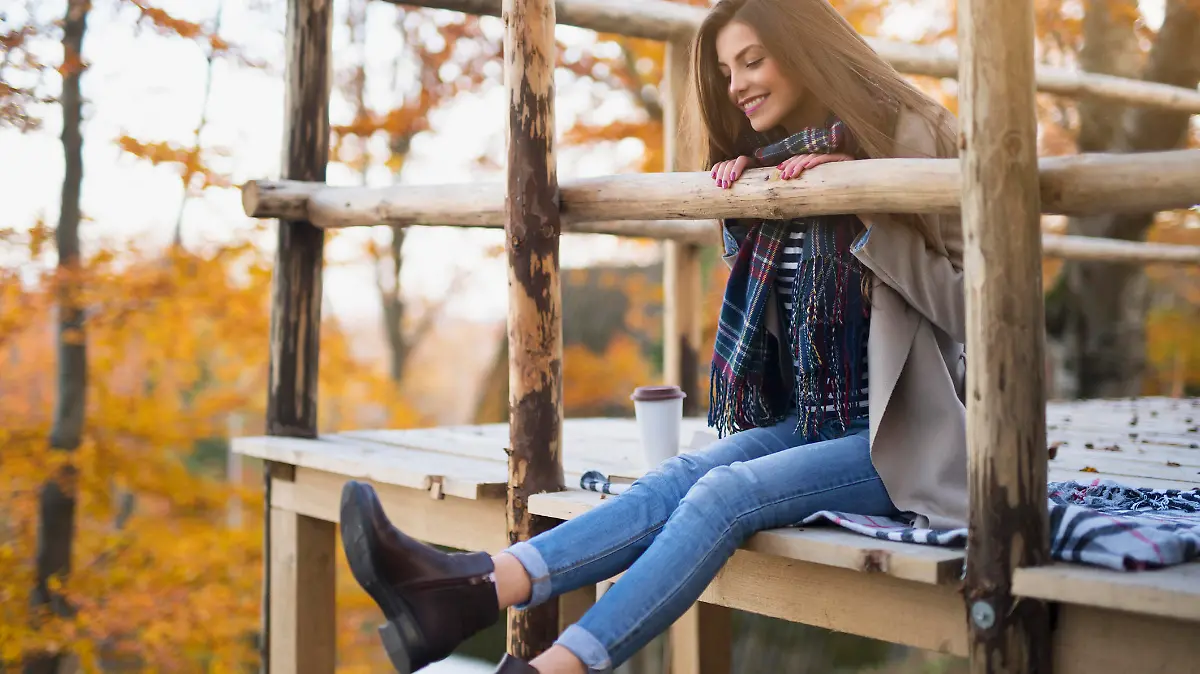 Beautiful young woman sitting on the wooden platform, having fun and enjoying the beautiful autumn environment