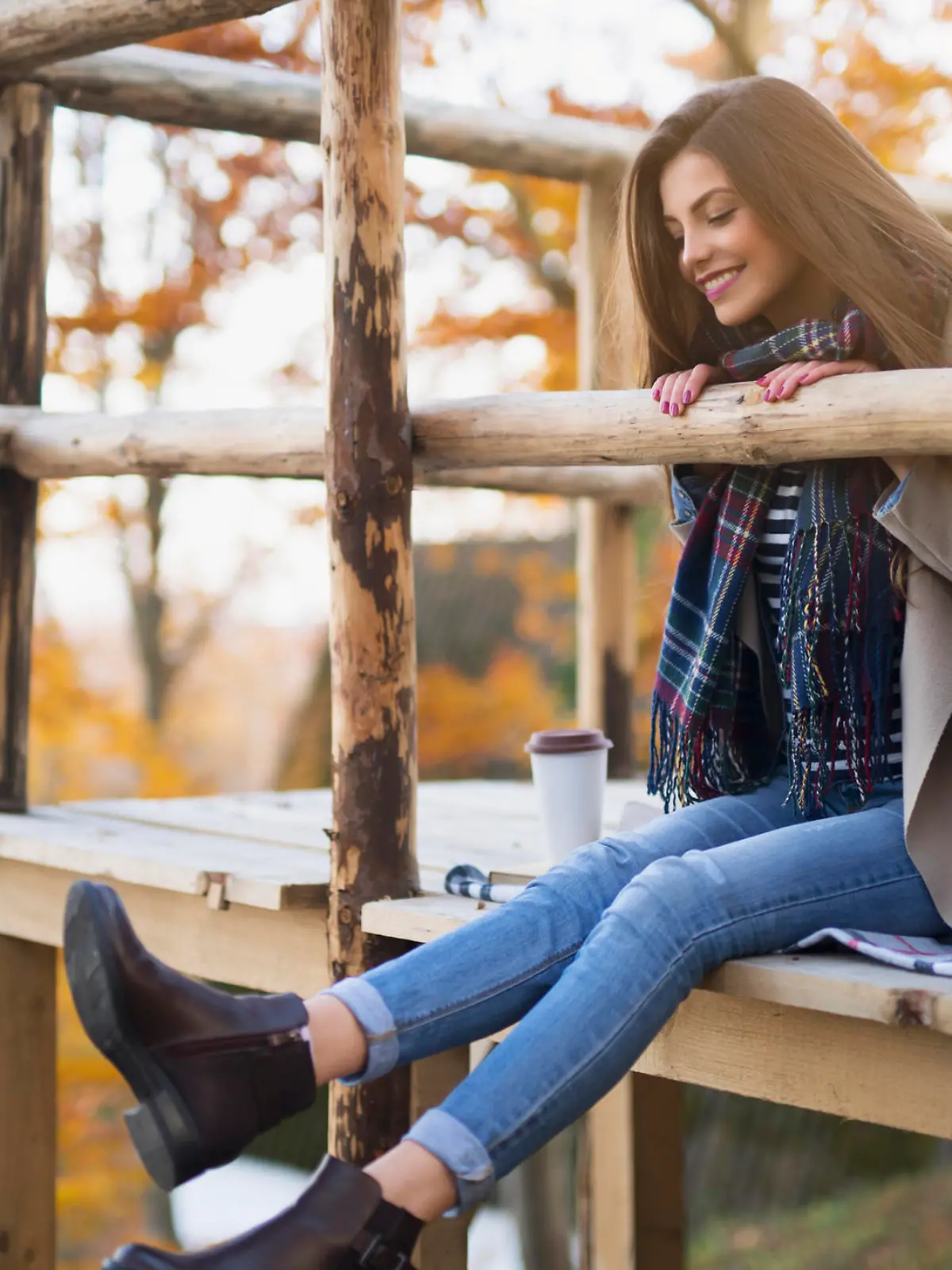 Beautiful young woman sitting on the wooden platform, having fun and enjoying the beautiful autumn environment