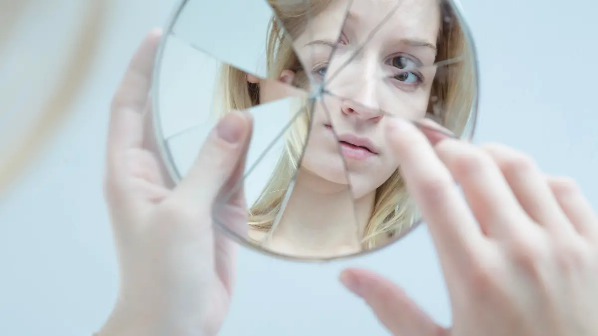 Insecure pretty young woman holding broken mirror