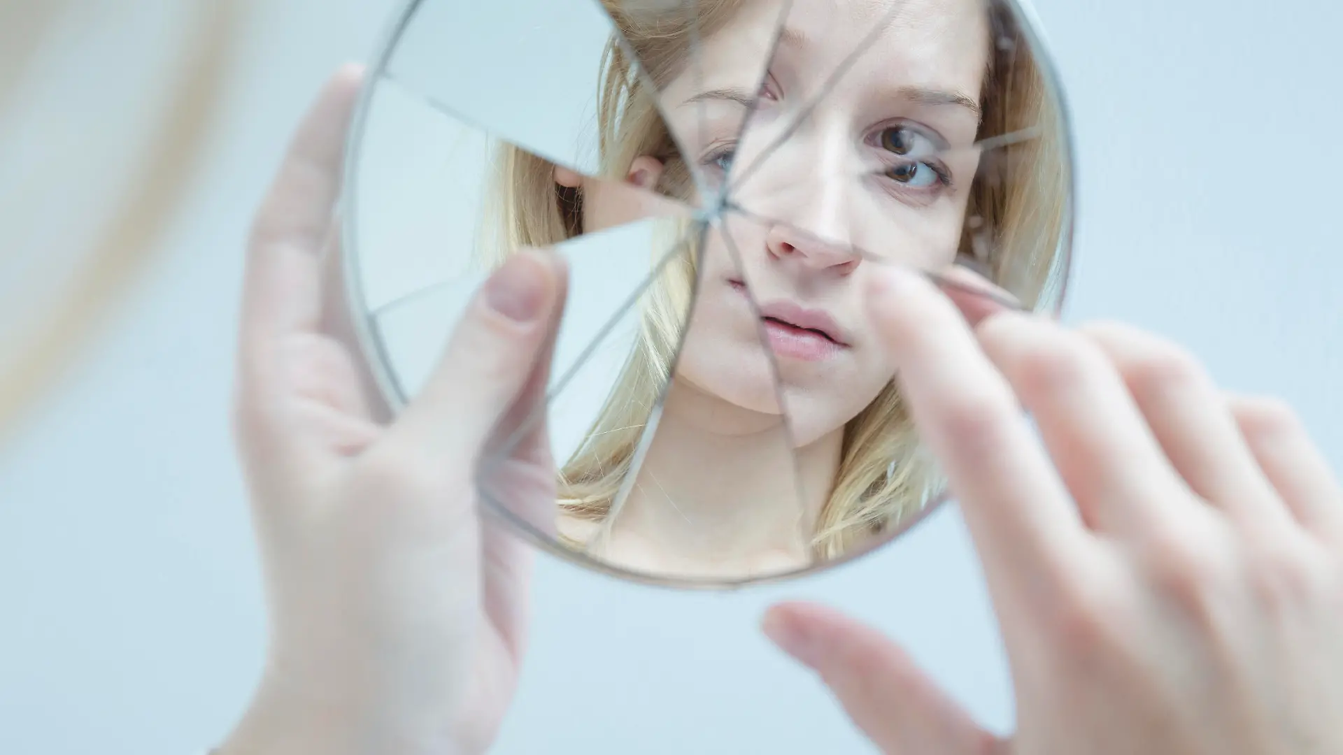 Insecure pretty young woman holding broken mirror