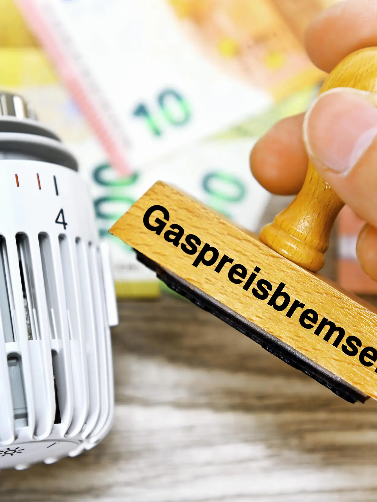  FOTOMONTAGE, Hand hält Stempel mit Aufschrift Gaspreisbremse neben Heizungsthermostat *** PHOTOMONTAGE, hand holding stamp with inscription gas price brake next to heating thermostat