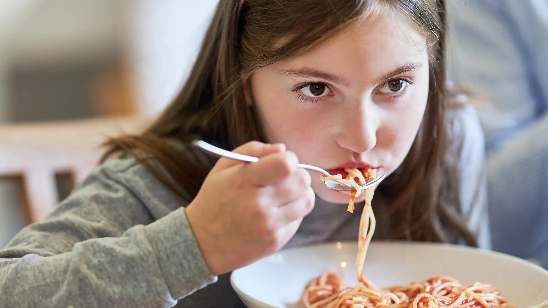 Hungriges Kind beim Spaghetti essen mit Tomatensauce beim Abendessen