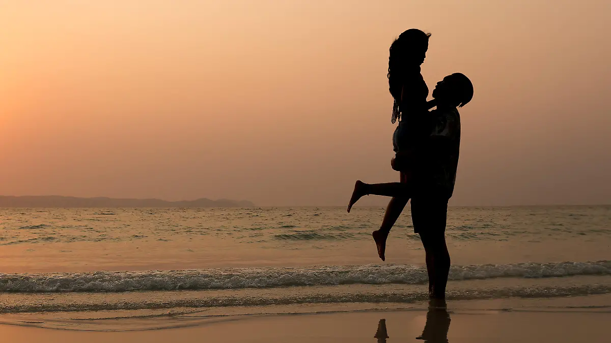 couple asian man lifting woman on the beach silhouette at sunset