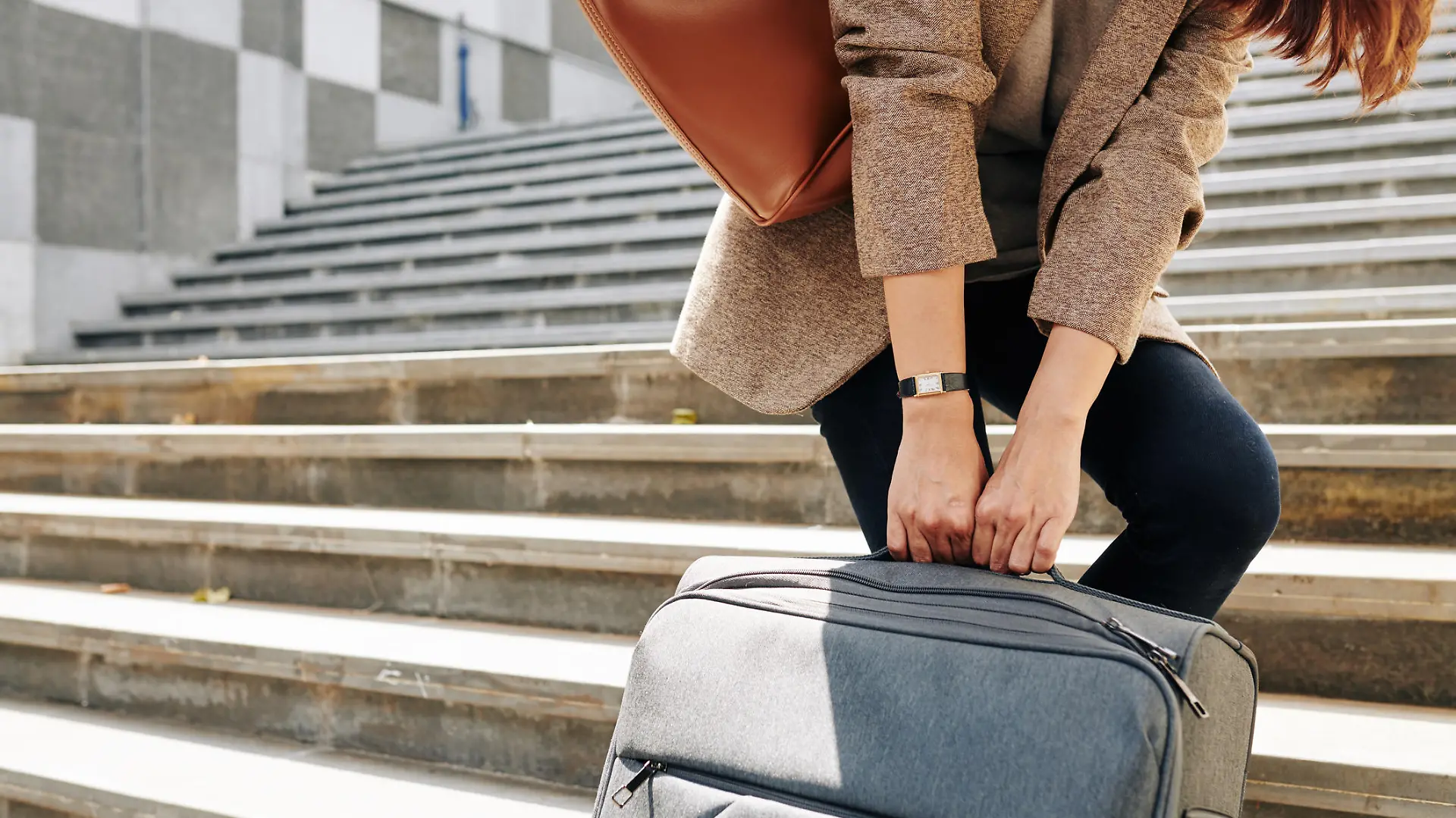 Cropped image of woman pulling big suitcase when walking up the stairs to railway station