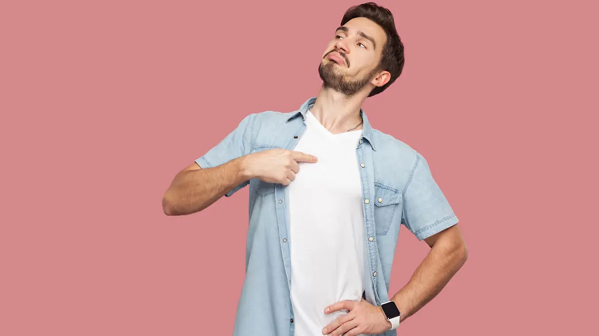 This is me. Portrait of proud haughty handsome bearded young man in blue casual style shirt standing, looking away and pointing himself. indoor studio shot, isolated on pink background.
