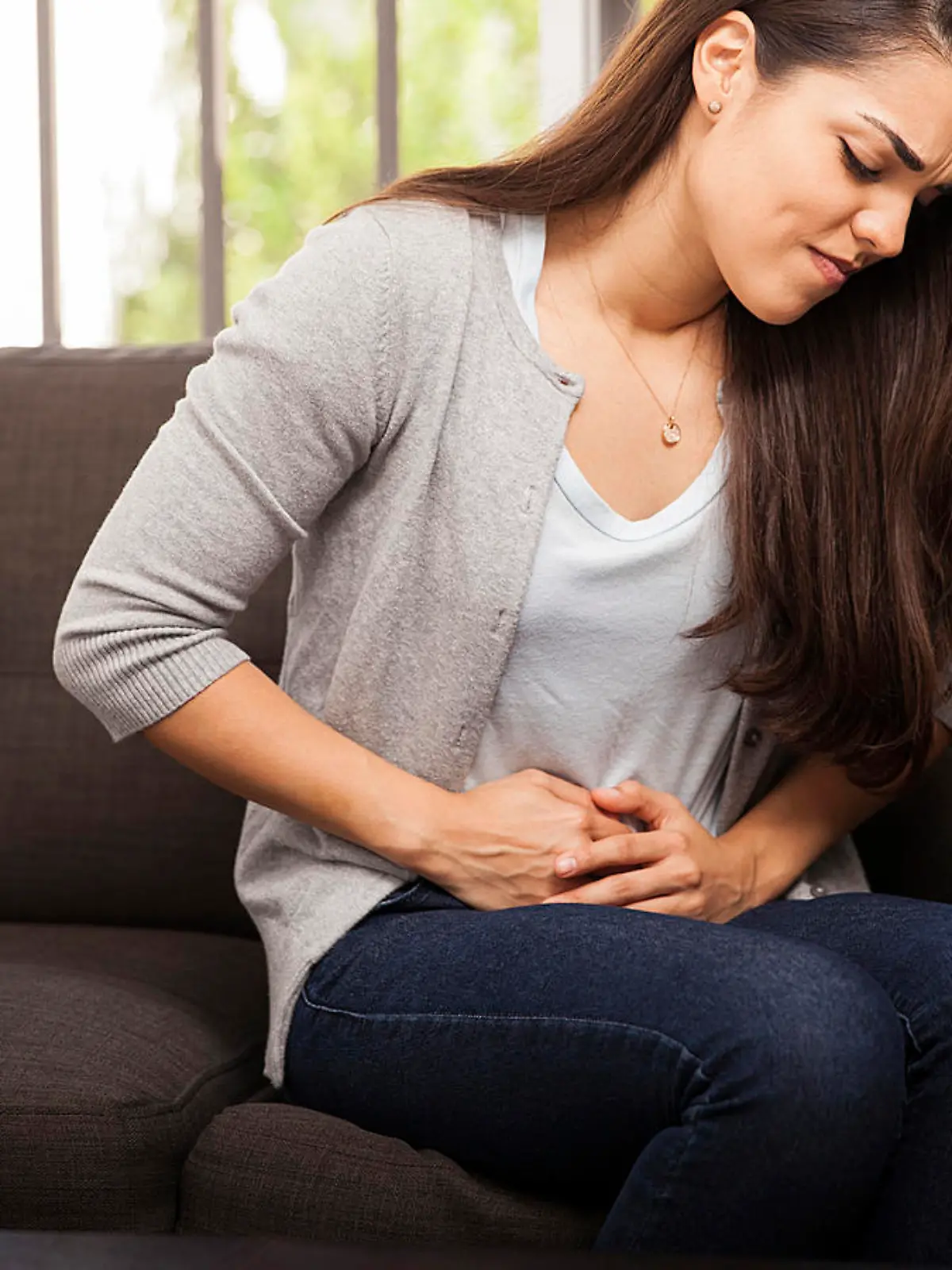 Young Hispanic woman sitting in a couch at home and suffering from colics