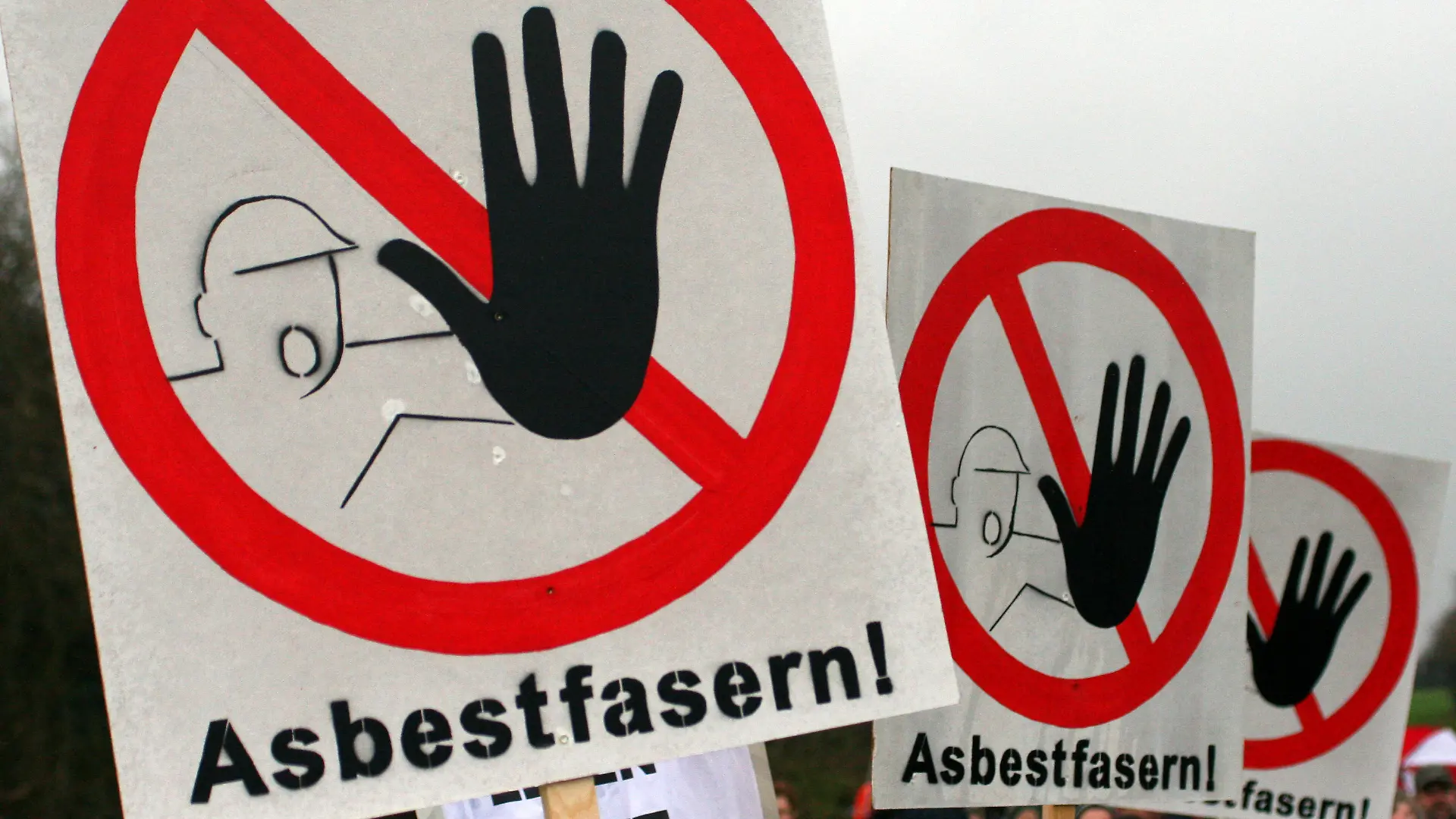 ARCHIV - 27.11.2011, Rondeshagen: Warnschilder vor Asbestfasern sind während einer Demonstration zu sehen. Das gesundheitsgefährdende Material Asbest schlummert im Verborgenen, rund ein Viertel aller Gebäude mit Bau- oder Sanierungsjahr vor 1994 könnte belastet sein. Jüngst wurde in Hamburg mehrfach Alarm geschlagen. (zu dpa «Gefahrenquelle Asbest: Altlasten schlummern noch immer in Gebäuden») Foto: Daniel Bockwoldt/dpa +++ dpa-Bildfunk +++