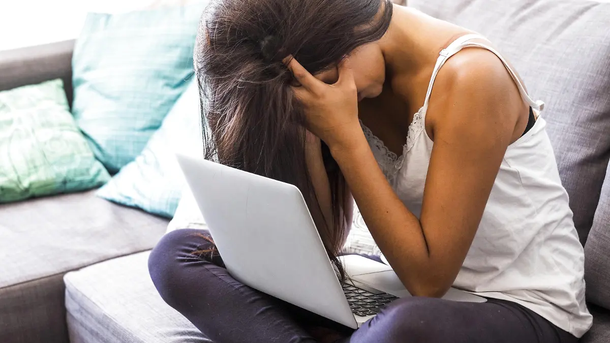 Stressed teenage girl with head in her hands sitting on the couch with laptop model released Symbolfoto property released PUBLICATIONxINxGERxSUIxAUTxHUNxONLY SIPF000742