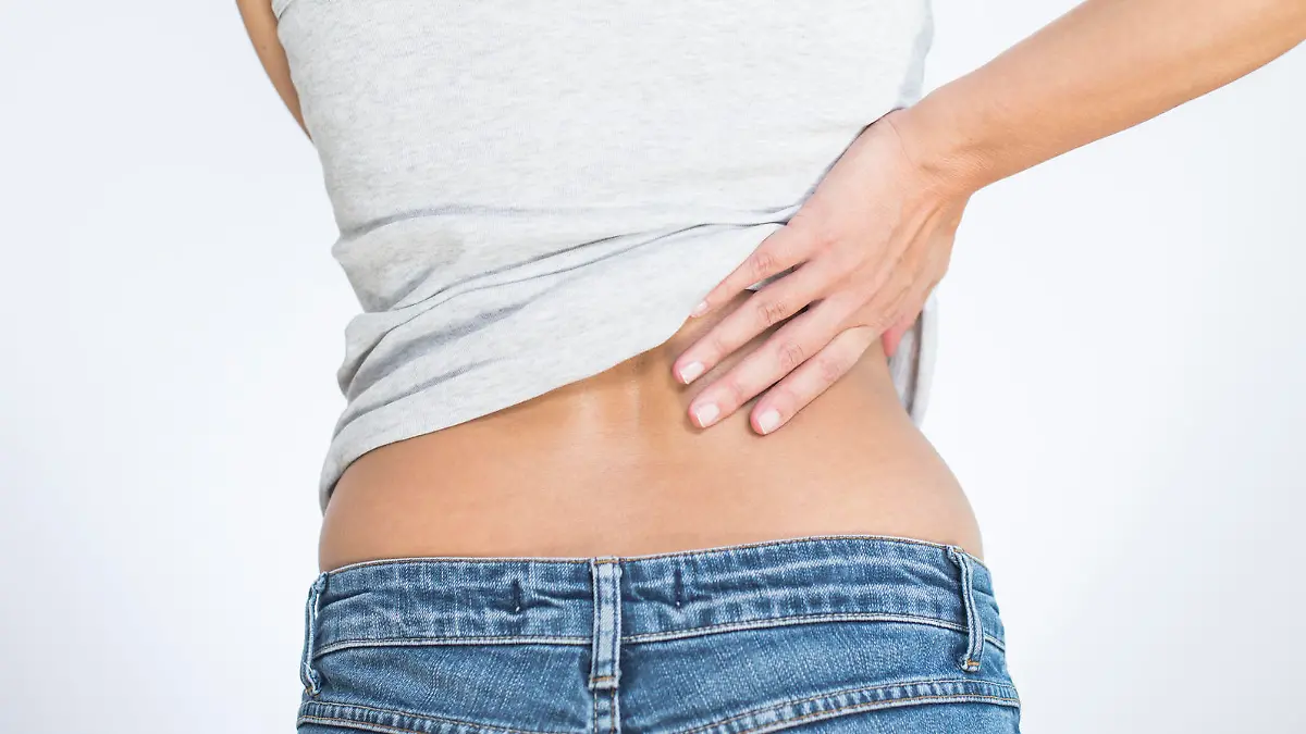 Rear view of a woman with lower back pain clutching her hands to her back and spine to relieve the ache in her muscles or spinal vertebrae and discs brought on by stress, injury or disease