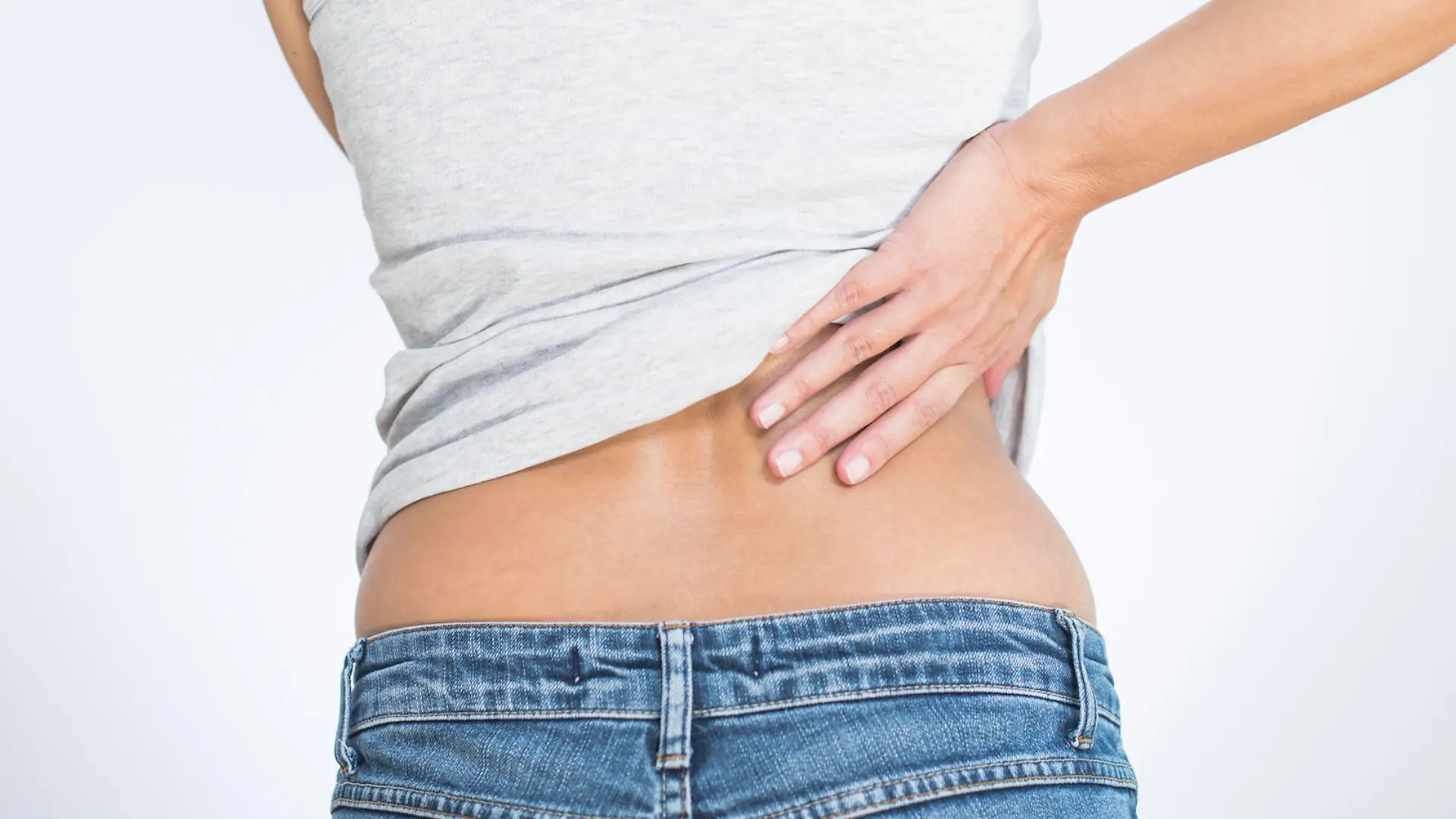 Rear view of a woman with lower back pain clutching her hands to her back and spine to relieve the ache in her muscles or spinal vertebrae and discs brought on by stress, injury or disease