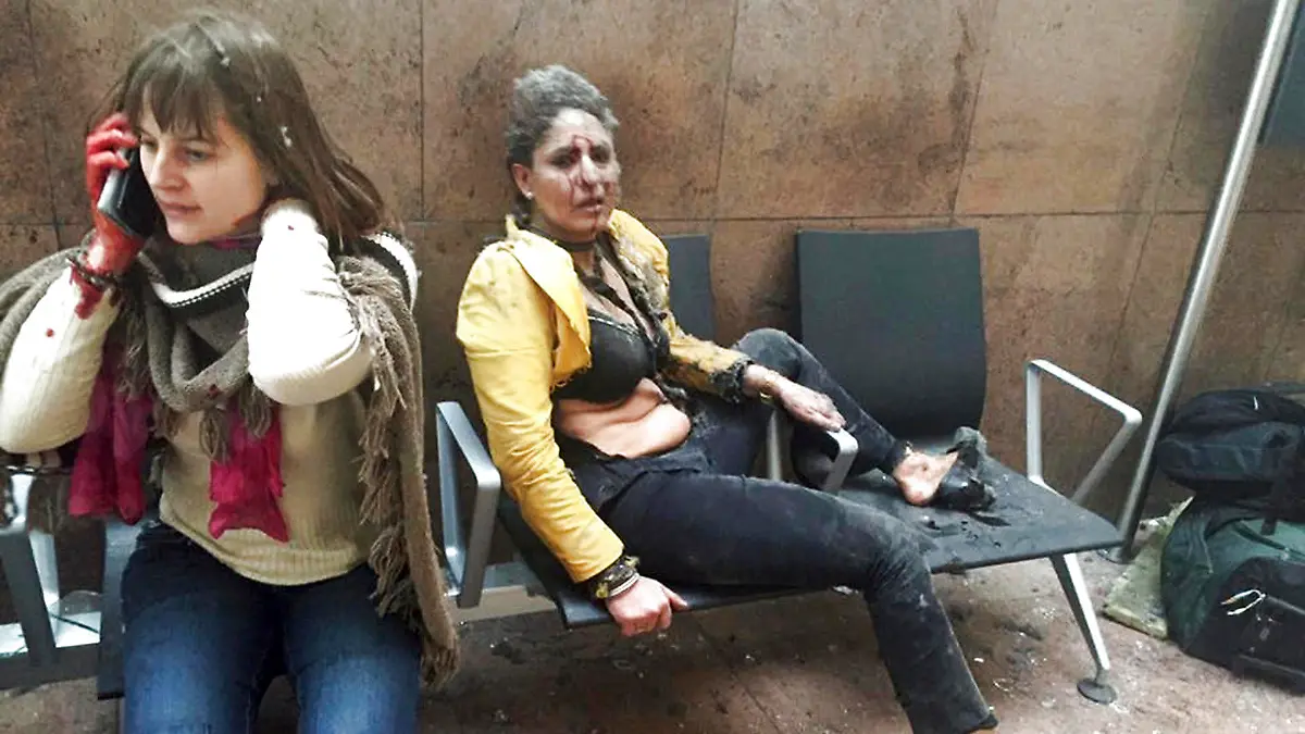 ARCHIV - Die indische Stewardess Nidhi Chaphekar (r) sitzt am 22.03.2016 unmittelbar nach dem Anschlag auf den Flughafen von Brüssel (Belgien) blutüberströmt und geschockt auf einer Flughafenbank. Die belgische Königin Mathilde und König Philippe empfangen Chaphekar am 20.03.2017 in Brüssel. Foto: Ketevan Kardava/AP/dpa +++(c) dpa - Bildfunk+++
