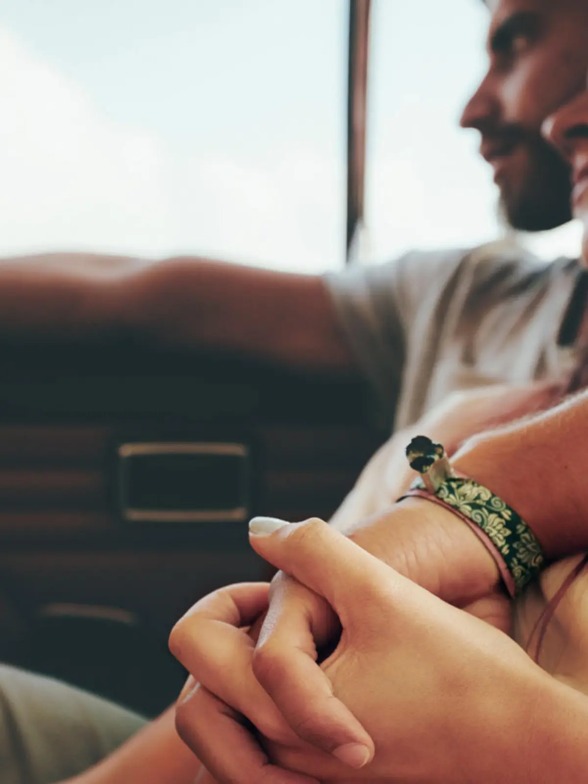 Affectionate young couple sitting in back seat of a car going on road trip. Focus on couple holding hands.