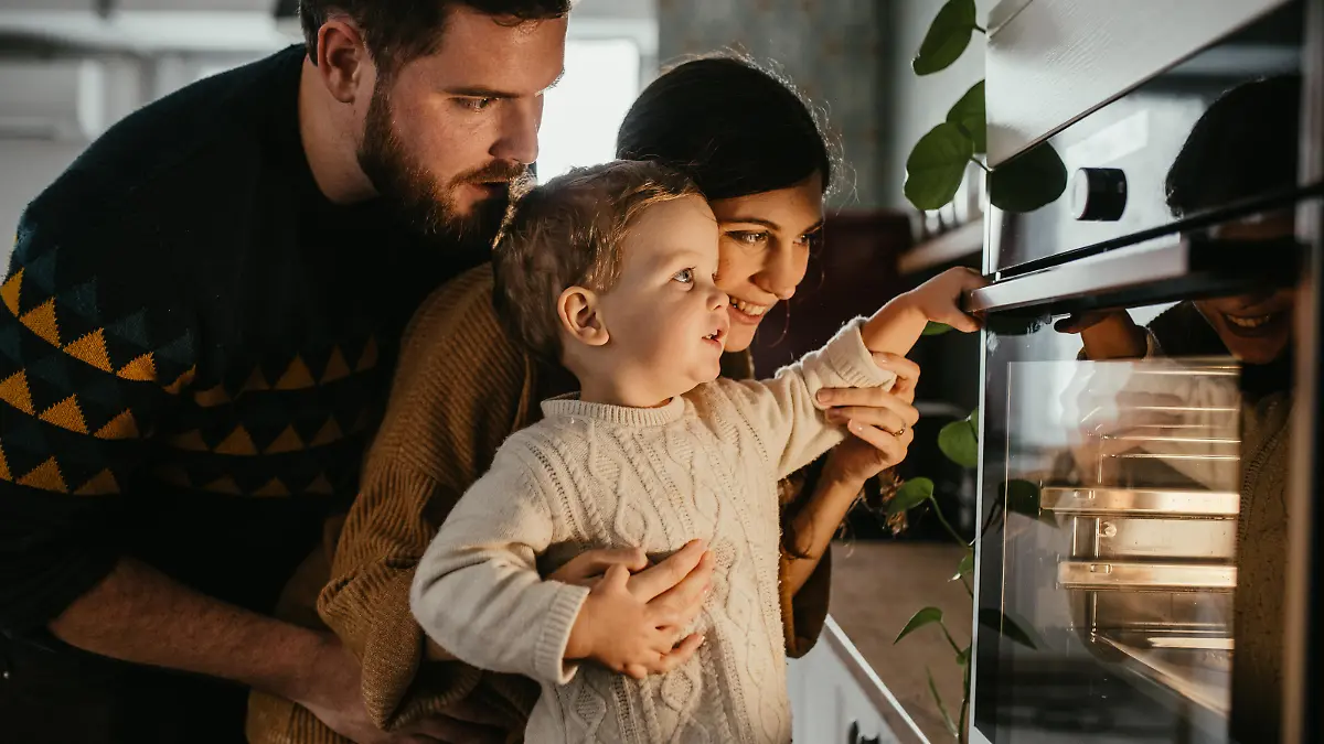 Young family with son is looking in the oven and waiting for their meal to be done.