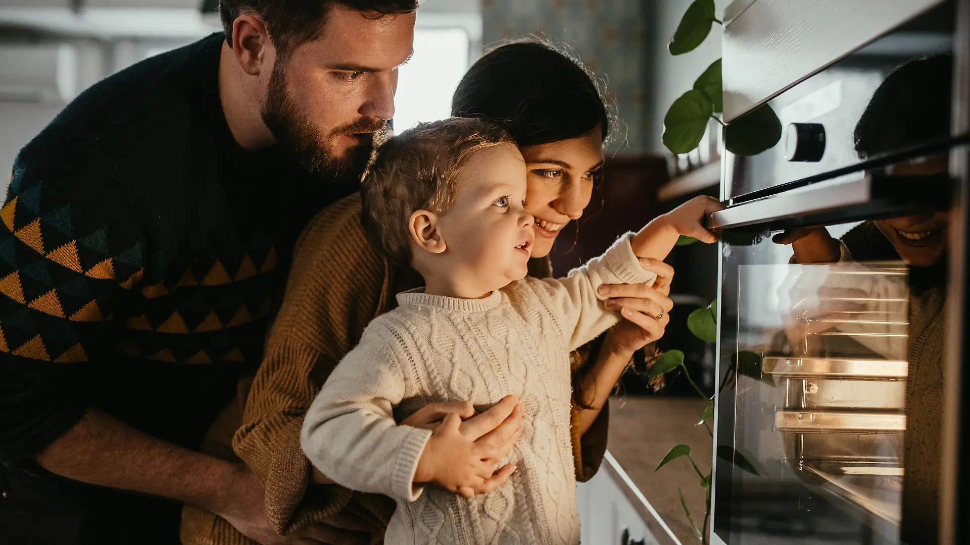 Young family with son is looking in the oven and waiting for their meal to be done.