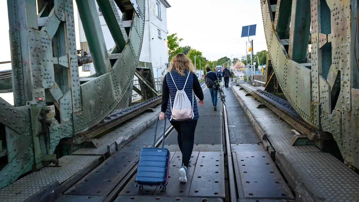 PRODUKTION - 25.09.2022, Schleswig-Holstein, Boren: Eine Frau läuft mit einem Koffer über die Lindaunisbrücke. Normalerweise fahren Züge über die Schleibrücke bei Lindaunis. Seit Mitte September aber heißt es für Fahrgäste: Austeigen und zu Fuß die Schlei passieren. Wegen Bauarbeiten ist die Brücke über die Schlei bei Lindaunis für Autos und Züge gesperrt. Foto: Jonas Walzberg/dpa +++ dpa-Bildfunk +++