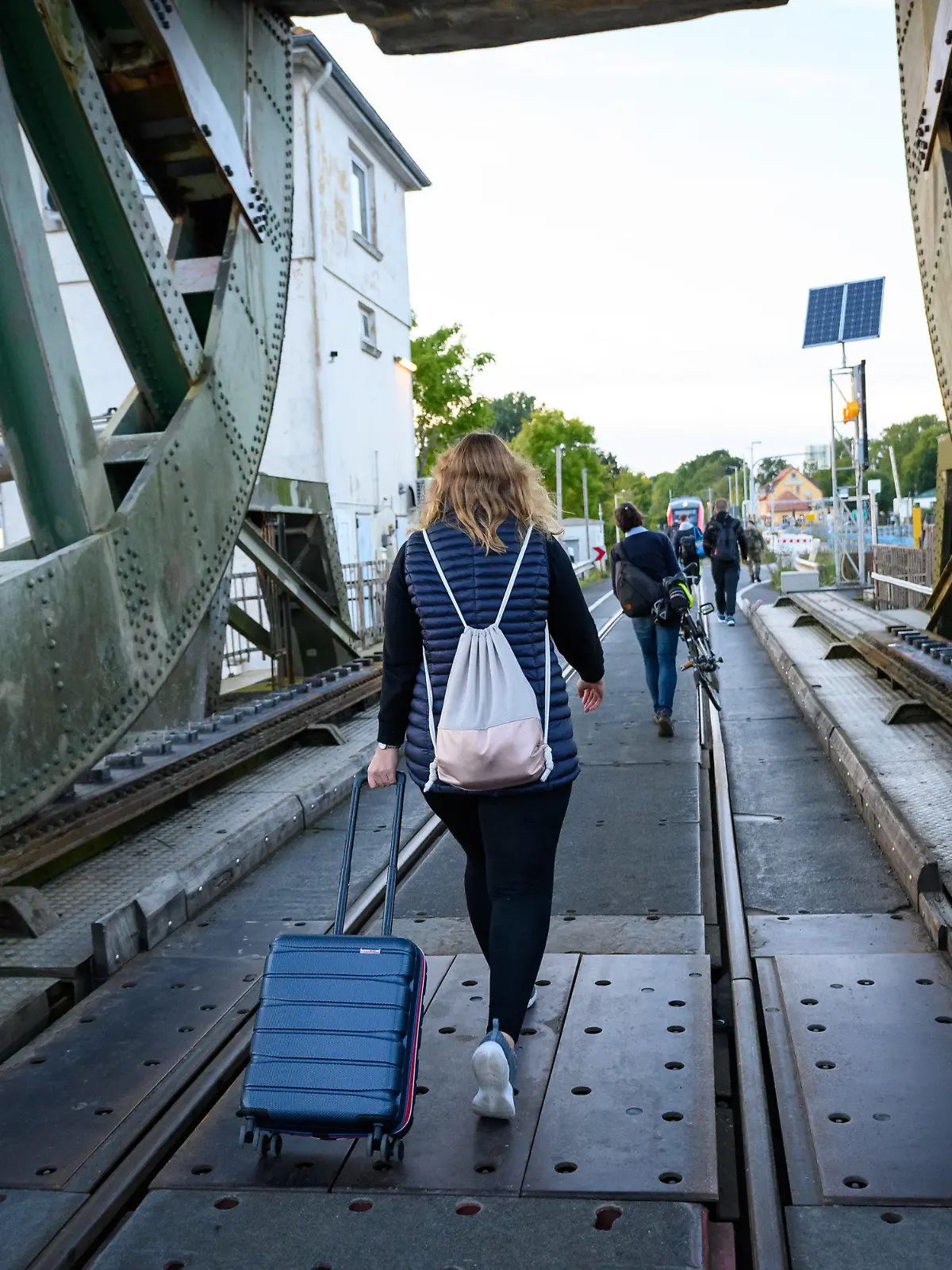 PRODUKTION - 25.09.2022, Schleswig-Holstein, Boren: Eine Frau läuft mit einem Koffer über die Lindaunisbrücke. Normalerweise fahren Züge über die Schleibrücke bei Lindaunis. Seit Mitte September aber heißt es für Fahrgäste: Austeigen und zu Fuß die Schlei passieren. Wegen Bauarbeiten ist die Brücke über die Schlei bei Lindaunis für Autos und Züge gesperrt. Foto: Jonas Walzberg/dpa +++ dpa-Bildfunk +++