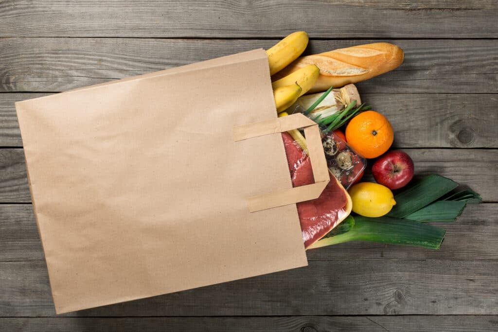 Different Food In Paper Bag On Wooden Background Close Up.