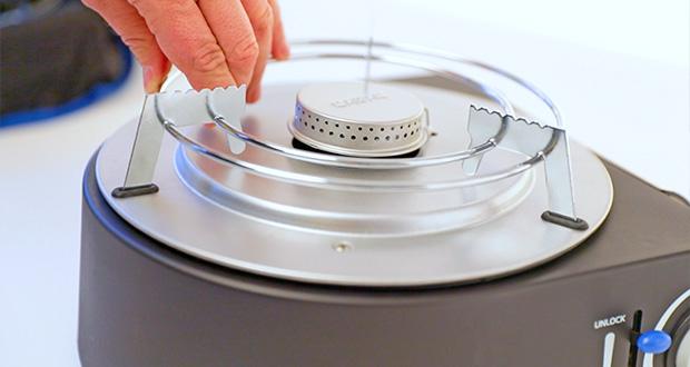 Hand setzt eine Metallhalterung über den Brenner eines mobilen Campinggrills.